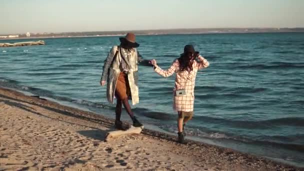 Beste vrienden houden handen en lopen langs het strand bij zonsondergang. de meisjes zijn genieten van een warme herfst dag — Stockvideo