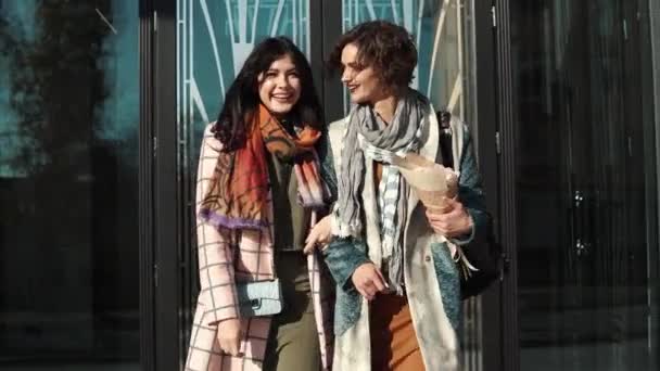 Novias abrazándose y sonriendo en el fondo de la arquitectura moderna. chica en abrigo de otoño posando en cámara. Los amigos pasan tiempo juntos — Vídeo de stock