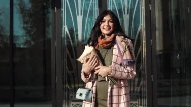 yakın çekim portre ayarı güneş ışınlarının içinde şık bir genç kadın. bir şehir arka plan güzel kız. bir buket ile kız