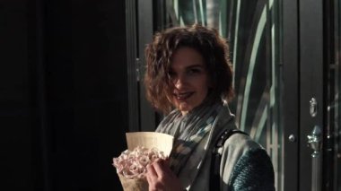 yakın çekim portre ayarı güneş ışınlarının içinde şık bir genç kadın. bir şehir arka plan güzel kız. bir buket ile kız