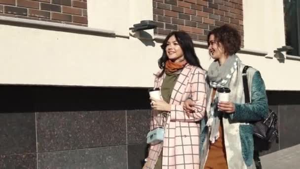Flickvänner på en promenad. två unga vackra kvinnor vandrar runt i staden som håller kaffe. — Stockvideo