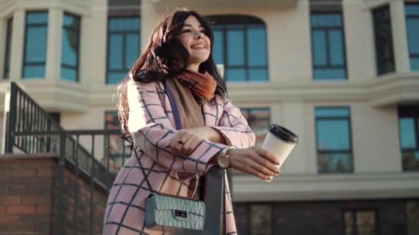 Красивая девушка пьет кофе на улице. Портрет привлекательной молодой женщины в пелто. Девушка улыбается и наслаждается теплым осенним днем — стоковое видео