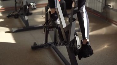 Kızlar bacaklar yakın çekim. Sporcumuz spor salonunda egzersiz bisikleti pedal açar.