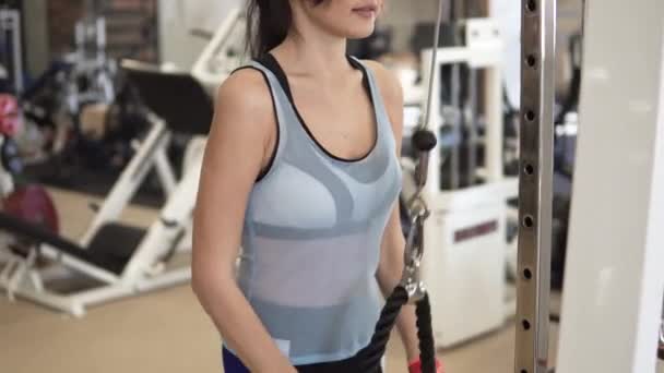Αθλητής κάνει ασκήσεις για τα triceps στο μηχάνημα στο γυμναστήριο. κορίτσι σε αθλητικά είδη για την εκπαίδευση — Αρχείο Βίντεο
