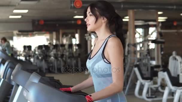 Νεαρή γυναίκα περπατά σε διάδρομο στο γυμναστήριο. καρδιο ασκήσεις στο γυμναστήριο — Αρχείο Βίντεο