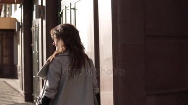 sevimli genç kadın bir ceket ve gülümsüyor sonbahar şehirde size yürür. modern mimarinin bir arka plan üzerinde şirin kız. ağır çekim