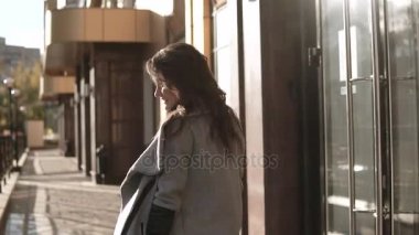 sevimli genç kadın bir ceket ve gülümsüyor sonbahar şehirde size yürür. modern mimarinin bir arka plan üzerinde şirin kız. ağır çekim