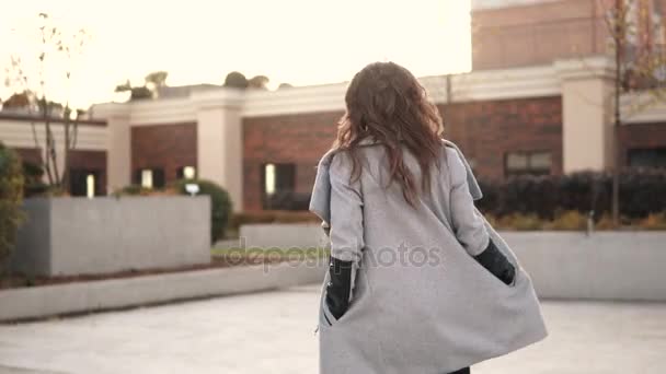 Porträt einer attraktiven jungen Frau im Herbstmantel vor dem Hintergrund urbaner Architektur — Stockvideo