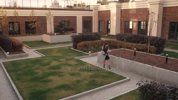 Charmiga unga kvinna går genom hösten staden i en kappa och ler. Söt tjej på en bakgrund av modern arkitektur. — Stockvideo