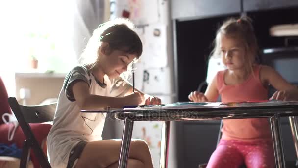 Niños dibujan con lápices en casa sentados a la mesa. dos niñas hermana dibujar juntos en la cocina — Vídeo de stock