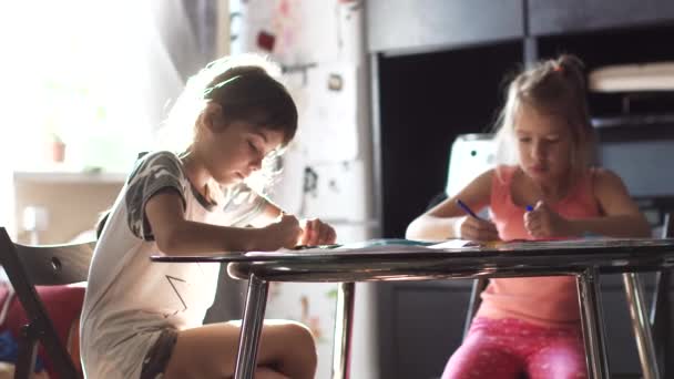 Dos hermanas de 6 y 7 años dibujando juntas sentadas a la mesa. niños dibujan con lápices de colores al sol — Vídeo de stock