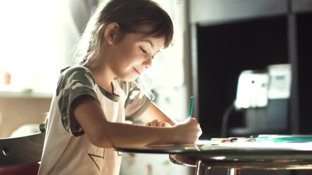 Dessin de petite fille avec des crayons à la maison assis à la table. l'enfant au soleil du matin — Video