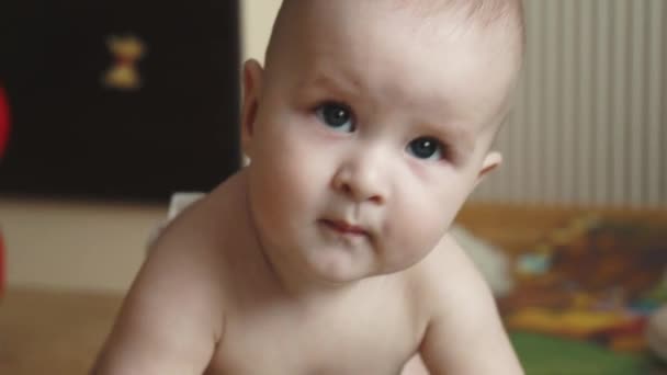 Little baby 1 year old close-up. child lies on the floor of the house. little boy looks at camera and smiles — Stock Video