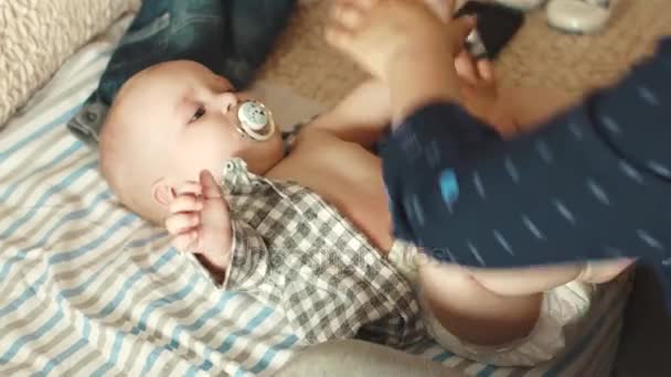 엄마는 그녀의 작은 아들에 셔츠에 넣습니다. 어머니는 자식 처리합니다. 아기는 그의 입에 젖꼭지를 보유 — 비디오
