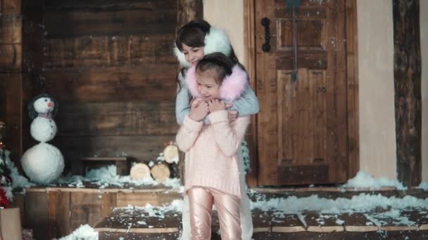 Natale o Capodanno. I bambini in abiti invernali leggeri si abbracciano. Due bambine sotto il portico della casa. rallentatore — Video Stock