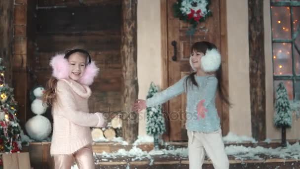 Natal ou Ano Novo. As crianças na roupa de inverno leve dão abraços um a outro. Duas meninas no alpendre da casa. câmara lenta — Vídeo de Stock