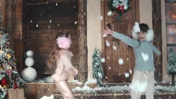 Kerstmis of Nieuwjaar. gelukkige kinderen, is overgeven van sneeuw. de kinderen genieten van de kerstvakantie. Twee kleine meisjes op de veranda van het huis. Slow motion — Stockvideo