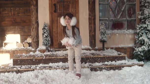 Weihnachten oder Neujahr. Porträt eines Kindes in Weihnachtsdekoration. kleines Mädchen mit Pelzkopfhörer wirft den Schnee in die Höhe und dreht sich fröhlich. Zeitlupe — Stockvideo