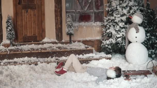 Natale o Capodanno. bambino scherza intorno e si trova nella neve artificiale. ritratto di un bambino in addobbi natalizi. rallentatore — Video Stock