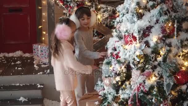 Kerstmis of Nieuwjaar. twee zusjes kijken naar het nieuwe jaar boom. kinderen in de achtergrond van kerstversiering — Stockvideo