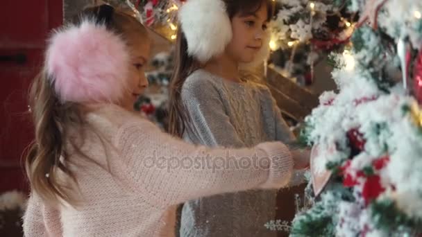Karácsony vagy újév. két kicsi nővér keres az újévi fa. gyermekek, a háttérben a karácsonyi díszek — Stock videók