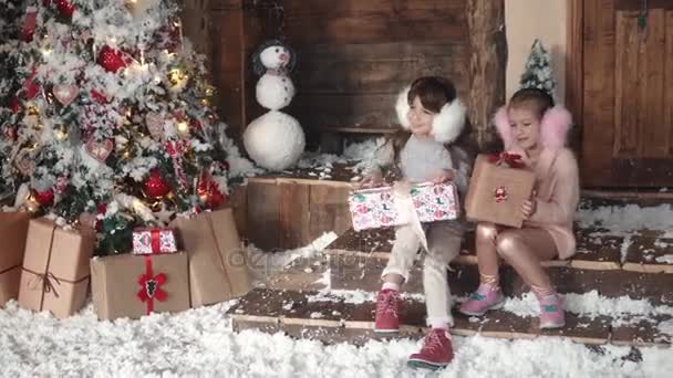 Weihnachten oder Neujahr. Kinder betrachten Geschenke in wunderschönen Weihnachtsboxen. zwei kleine Mädchen auf einem Weihnachtsbaum Hintergrund — Stockvideo
