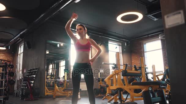 Deportista se calienta antes de entrenar en el gimnasio. una chica con una figura apretada se dedica a los deportes — Vídeos de Stock