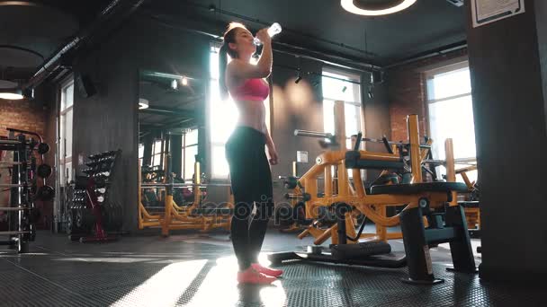 Девушка пьет воду во время занятий в тренажерном зале. девушка в спортивной одежде на солнце — стоковое видео