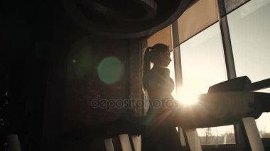 bir kız bir koşu bandı üzerinde silüeti. içme suyu bir şişe eğitim kızdır. genç kadın spor salonunda bir koşu bandı üzerinde yürür. spor salonunda kardiyo egzersizleri