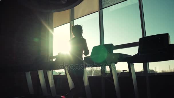 Entraînement cardio dans la salle de gym. silhouette d'une fille sur un tapis roulant. jeune fille sportive courant sur le tapis roulant à la salle de gym. athlète en vêtements de sport — Video