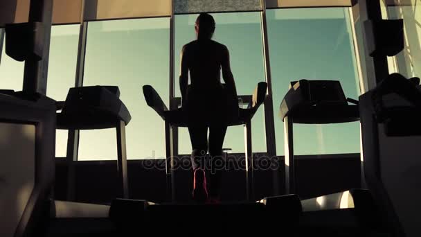 Silhouette d'une fille sur un tapis roulant. jeune femme marche sur un tapis roulant à la salle de gym. exercices cardio dans la salle de gym — Video