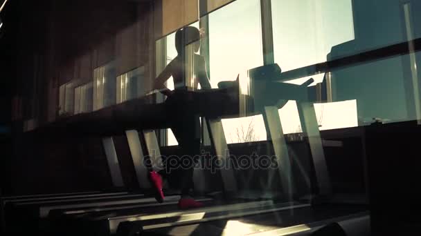 Entraînement cardio dans la salle de gym. silhouette d'une fille sur un tapis roulant. jeune fille sportive courant sur le tapis roulant à la salle de gym. athlète en vêtements de sport — Video