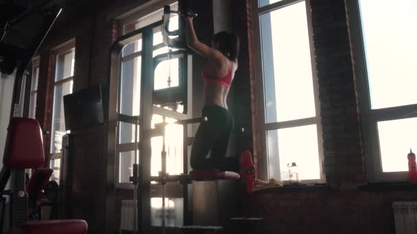 Mädchen in Sportbekleidung trainiert im Fitnessstudio. die Sportlerin zieht sich an der Latte hoch — Stockvideo