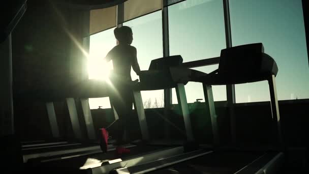 Cardio op de loopband. oefeningen voor gewichtsverlies. silhouet van een meisje op een loopband. sportieve meisje draait op de loopband in de sportschool. atleet in sportkleding — Stockvideo