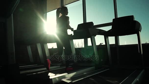 Cardio auf dem Laufband. Übungen zur Gewichtsabnahme. Silhouette eines Mädchens auf einem Laufband. junges sportliches Mädchen beim Laufen auf dem Laufband in der Turnhalle. Sportler in Sportbekleidung — Stockvideo