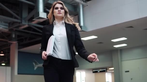 Confident business woman is walking along the production building. the manager is in a hurry to meet with clients or a business partner. woman in business suit holding documents in hands — Stock Video