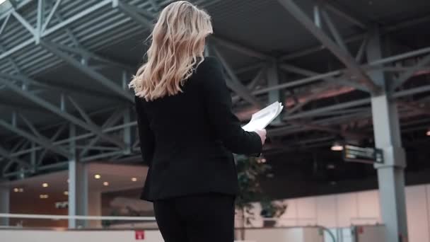 ビジネスの女性は、会議に急ぐ。ビジネス スーツの女性は、彼女の手で書類付きのビジネス センターを歩いています。背面図 — ストック動画