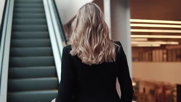 商务西装上的女人在大型商务中心的自动扶梯上升起。持有文件的商业妇女。后退视图 — 图库视频影像