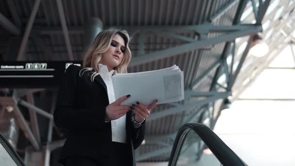 Женщина в деловом костюме спускается на эскалаторе в большом офисном здании. деловая женщина с документами — стоковое видео