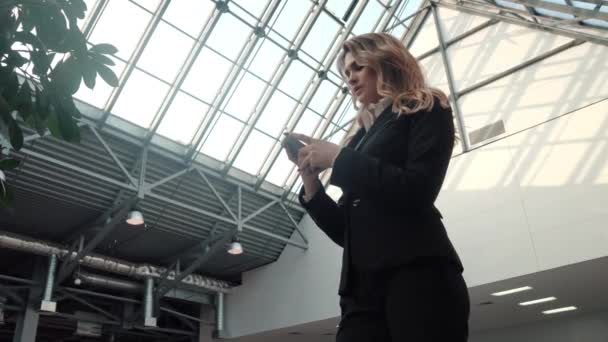 Young woman in a business suit uses a mobile phone. business woman is texting a message on the smartphone in the office building. — Stock Video