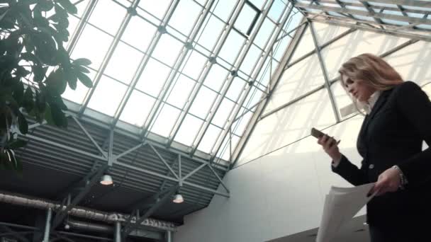 Business woman is texting a message on the smartphone in the office building. young woman in a business suit uses a mobile phone — Stock Video