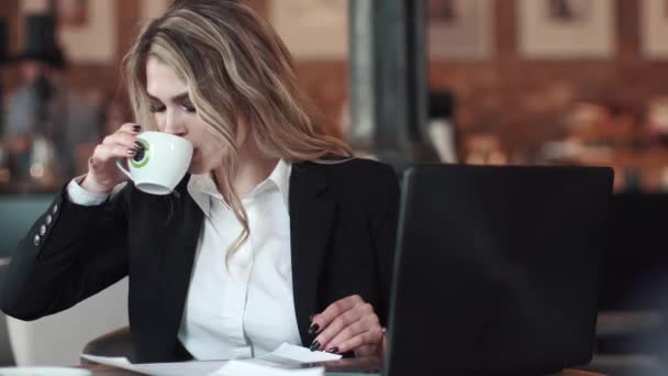 Деловая женщина пьет кофе в кофейне и работает с ноутбуками и бумажными документами — стоковое видео