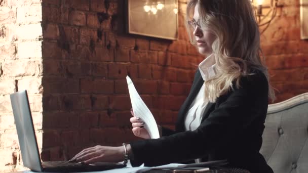 Деловая женщина работает в кафе на ноутбуке. девушка в деловом костюме, работающая с документами в неформальной обстановке — стоковое видео