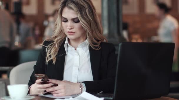 ビジネス女性は携帯電話でメッセージのテキスト メッセージです。テーブルに座ってコーヒー ショップで働くビジネス服で魅力的な女の子 — ストック動画