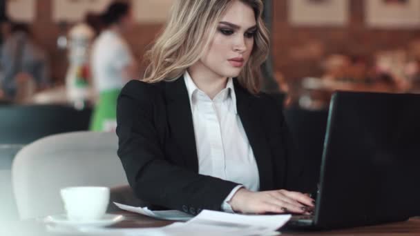 Uma mulher de negócios trabalha num portátil sentado num café. uma menina atraente atende um telefonema — Vídeo de Stock