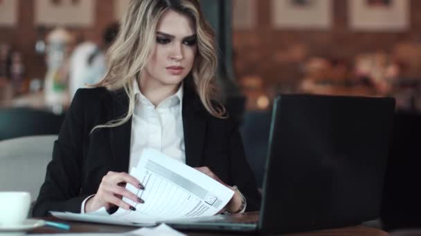 Business woman working with documents sitting at a table in a coffee shop. a girl in a business style to sign documents — Stock Video