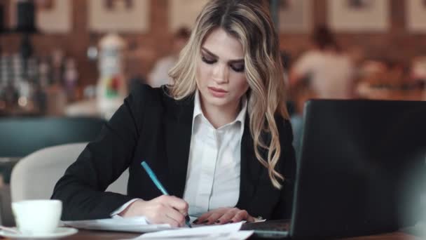 Biznes kobieta podpisuje dokumenty, siedząc przy stoliku w kawiarni. Dziewczyna w kurtkę i bluzka działa w nieformalnych meble. biznesowe makijaż i fryzurę — Wideo stockowe