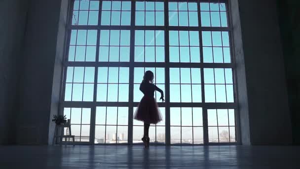 Silhuetten av en ballerina på en bakgrund av ett stort fönster. balettdansös spinning i pointe skor — Stockvideo