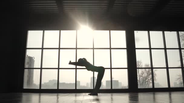 Joven chica flexible haciendo el calentamiento antes de entrenar en el fondo de una ventana grande. chica practicando yoga — Vídeo de stock