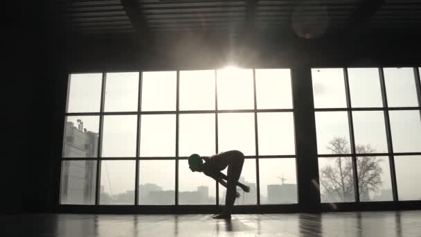 Silueta de un atleta sobre el fondo de una gran ventana. chica de deportes haciendo calentamiento antes del entrenamiento. mujer joven practicando yoga — Vídeos de Stock